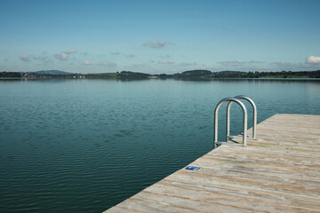 Obraz premium Wooden pier with a ladder leading into a calm lake. Concept of summer, relaxation, and nature.