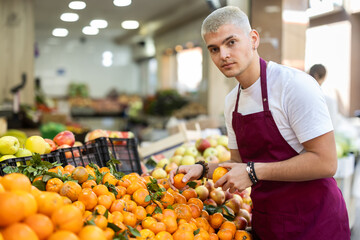 Working in supermarket - male salesman sorts through ripe tangerines on the display case
