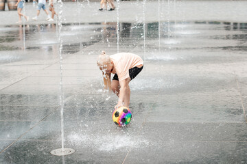 Child interacting with water and ball outdoors