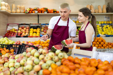 Shop assistants wrap halves of large watermelon in transparent membrane. Customer focus, meeting demand.