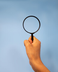 Hand holding magnifying glass on blue background with copy space