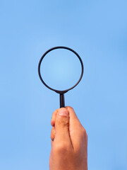 Hand holding magnifying glass on blue background for search and research concept