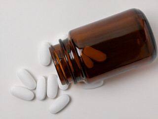 Brown glass medicine bottle with white tablets spilled on white background