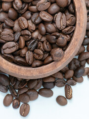 Close up of roasted coffee beans in wooden bowl on white background