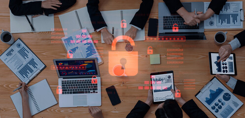 A secure business meeting featuring various professionals analyzing growth charts and digital data, emphasizing digital protection and teamwork in a collaborative environment. Trope