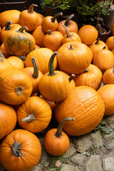 Vibrant orange pumpkins of various sizes are stacked together on a rustic stone surface, showcasing their unique shapes and textures in a seasonal autumn display
