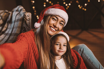 Capturing Happy Momets. Happy woman and cute little girl in santa claus hats taking festive selfie...