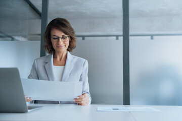 Focused mature latin hispanic business woman working on laptop computer reading financial document report in office. Accountant entrepreneur manager businesswoman doing paperwork using pc. Copy space