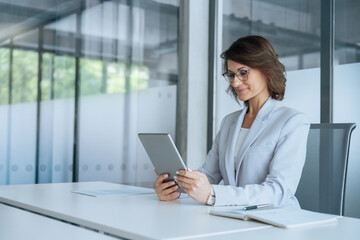 Latin mature adult professional business woman looking at online trade app. European businesswoman CEO holding digital tablet using tab application sitting at workplace desk in office. Copy space