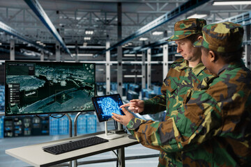 Military experts in data center reviewing drone surveillance feed using AI on tablet. Army units in high tech server room doing battlefield reconnaissance operations using artificial intelligence