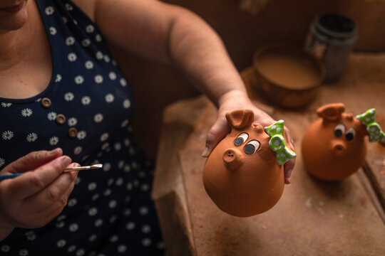 Female artisan painting clay piggy banks in pottery workshop