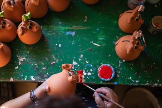 Female artisan painting clay piggy banks in pottery workshop