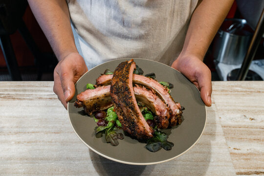 Pork ribs with salad served on a round plate inside a restaurant