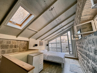 A Cozy Loft Bedroom Featuring Exposed Stone Walls and Bright Natural Light from Large Windows with Skylights, Perfect for Relaxing Getaways or Urban Living