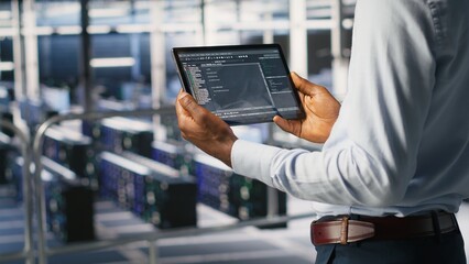 Data center admin checking code on tablet next to colleague reviewing AI visualizations in blurry background. IT experts use device to analyze neural networks outputs, ensuring stable gear operations