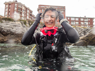 Scuba diver adjusting hair coming out of water near rocky coast