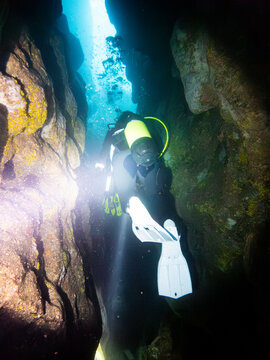 Scuba diver exploring narrow underwater cave with light beam