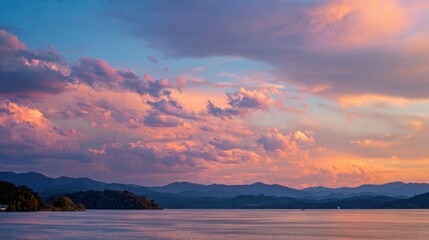 Fototapeta premium A stunning sunset casts warm colors over a calm lake surrounded by mountains. Soft clouds float in the sky as the sun descends creating a tranquil atmosphere for nature lovers.