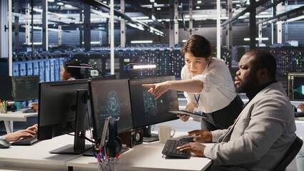 Server room manager supervise technician examining deep learning algorithms. Data center team leader and African american employee review performance dashboards of AI equipment rigs, camera A