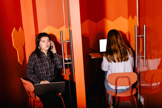 Female freelancers collaborating on laptops at individual cubicles