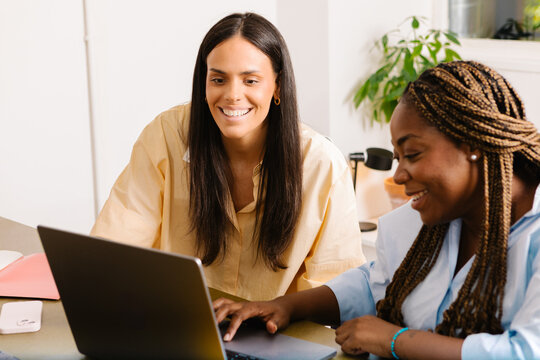 Female creatives collaborating and assisting each other over a laptop