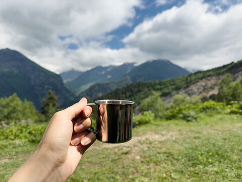 Anonymous hand holding simple metal cup in mountains
