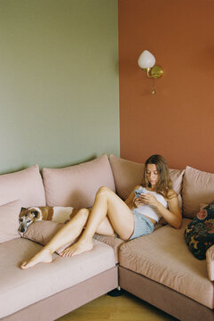 Woman Lounging with Dog While Using Phone at Home
