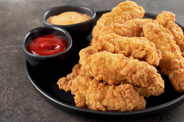 Crispy chicken breast strips with ketchup on a dark background. Close-up. Fast food.