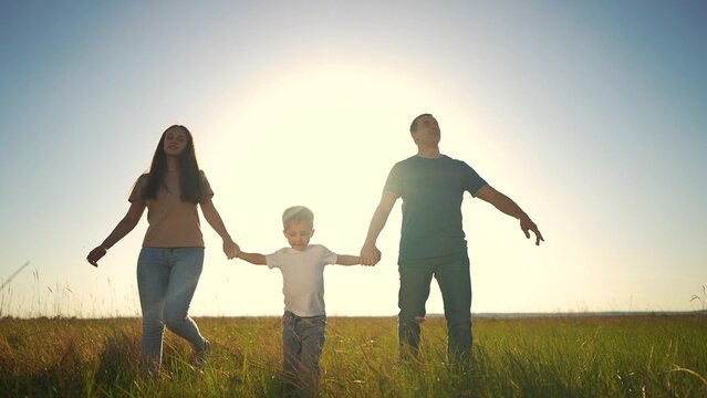 family walking together. outside people and family concept. happy family of three walking through a large field at beautiful sunset, mom and dad holding their son hands lifestyle - Powered by Adobe