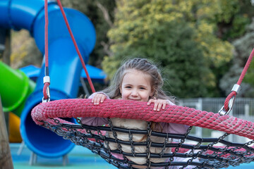 A happy girl swings on a swing at a bright playground. Playground and childhood