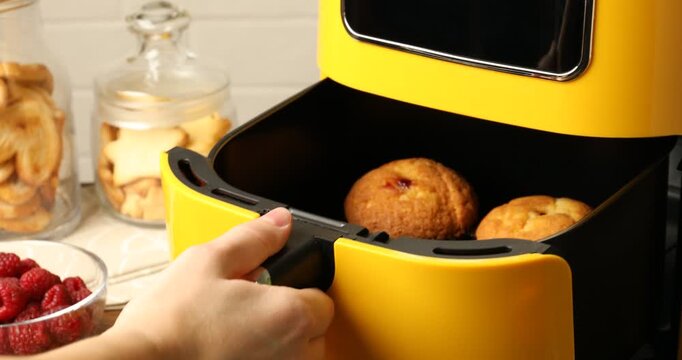 Woman opening air fryer with freshly baked muffins at wooden table, closeup