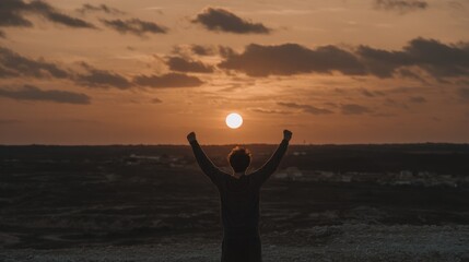 Fototapeta premium Person with arms raised towards the sunset, achieving a goal, sky view