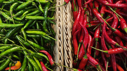 Fresh green and red chili peppers displayed side by side in a woven basket, showing vibrant color contrast and natural texture, symbolizing spice and flavor in cooking.