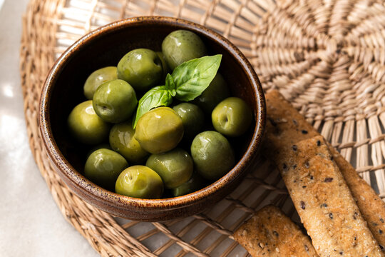 Bowl of Green Olives With Herbs and Crackers on Woven Mat