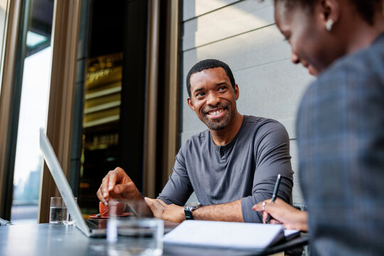 Business meeting: man smiles at colleague taking notes.