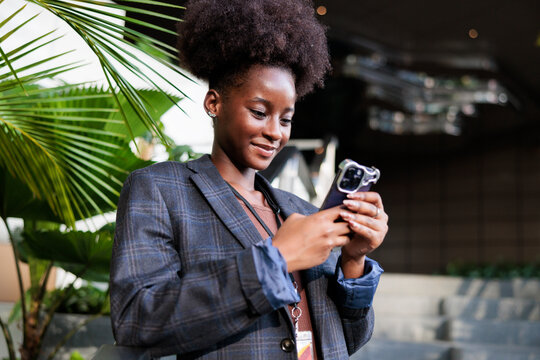 Woman in blazer smiles while using her phone.