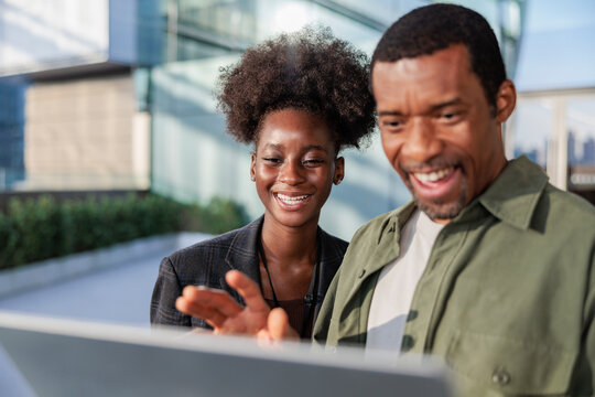 Two smiling people looking at a laptop outdoors.