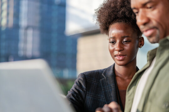 Business colleagues review laptop in front of city building.