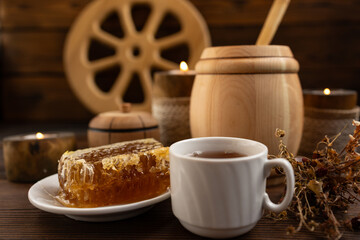 lose-up of a honeycomb on a white plate surrounded by a wooden barrel and a cup. a warm and rustic atmosphere. Bee honey.