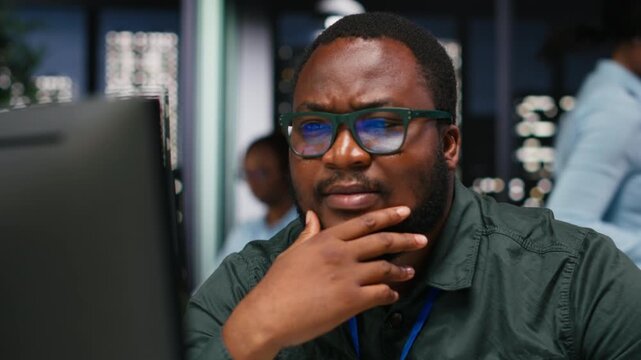 African american analyst wondering about possible solutions to a dilemma on computer, concentration to evaluate projections with logical deduction and intuitive observation at night. Camera B.