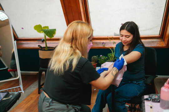 Tattoo artist cleaning fresh tattoo on client&rsquo;s arm