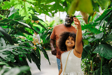 Curious girl reaching for tropical plant with grandfather