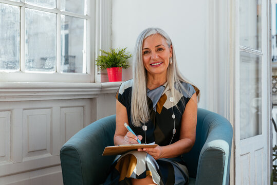 Smiling Senior Businesswoman Writing Notes while looking at camera