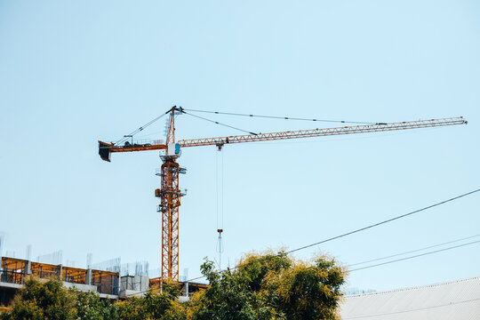 Construction crane near new building against blue clear sky.