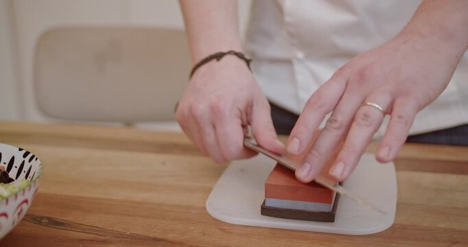 A chef sharpens a knife on a whetstone in preparation for dinner. Getting ready for meal preparation in a home kitchen.