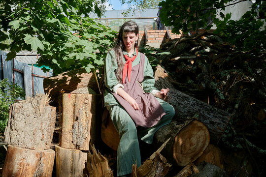 Woman sitting on a stack of logs in a rustic outdoor setting