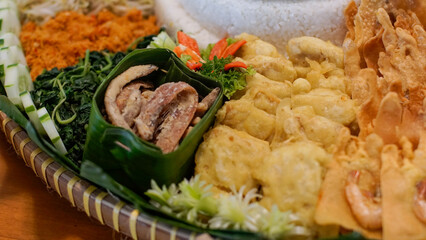 Indonesian traditional meal “Nasi Urap” served on banana leaf tray with white rice, seasoned grated coconut, fried tempeh, salted fish, shrimp crackers (rempeyek), and fresh vegetables