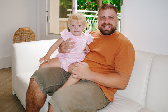 Father holding smiling baby daughter on white sofa