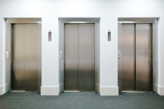 Three elevator doors closing in modern building lobby
