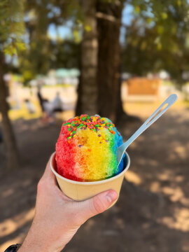 Hand Holding Rainbow Shaved Ice with Sprinkles Outdoors